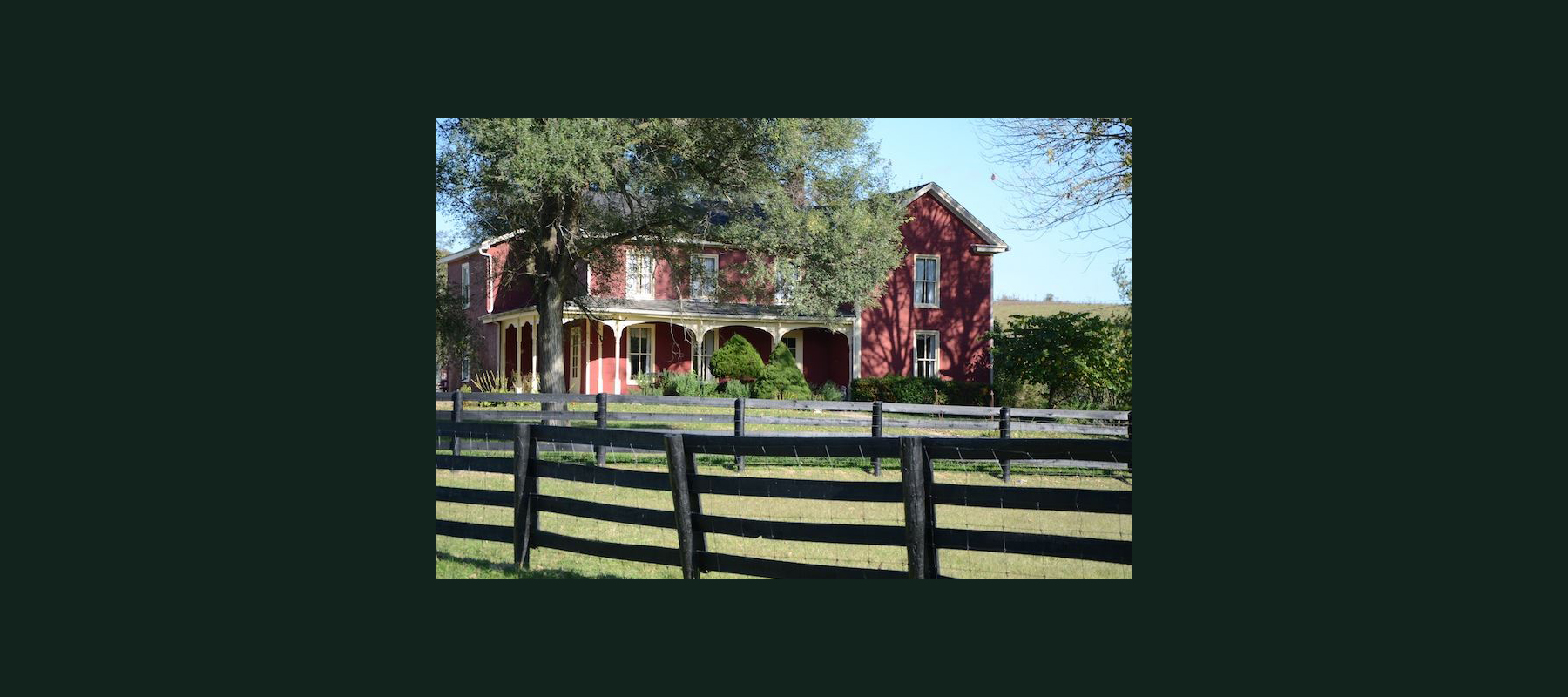 red brick home with black farm fences and cloudless sky